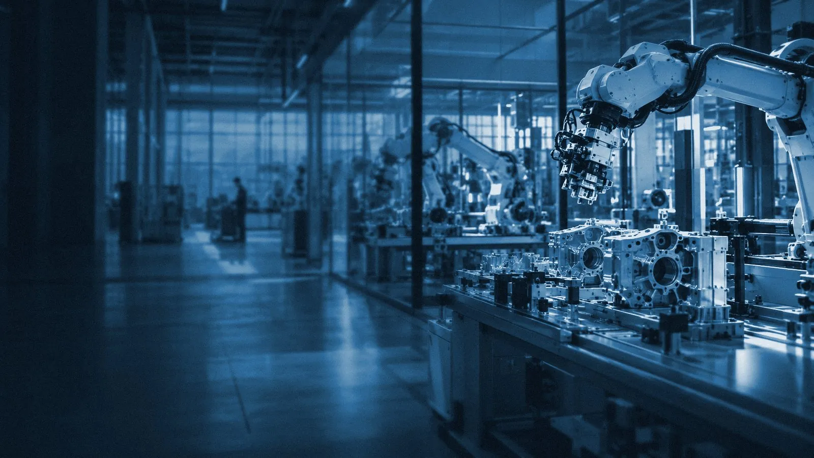 A robotic assembly cell on a factory floor, with a technician in the distance